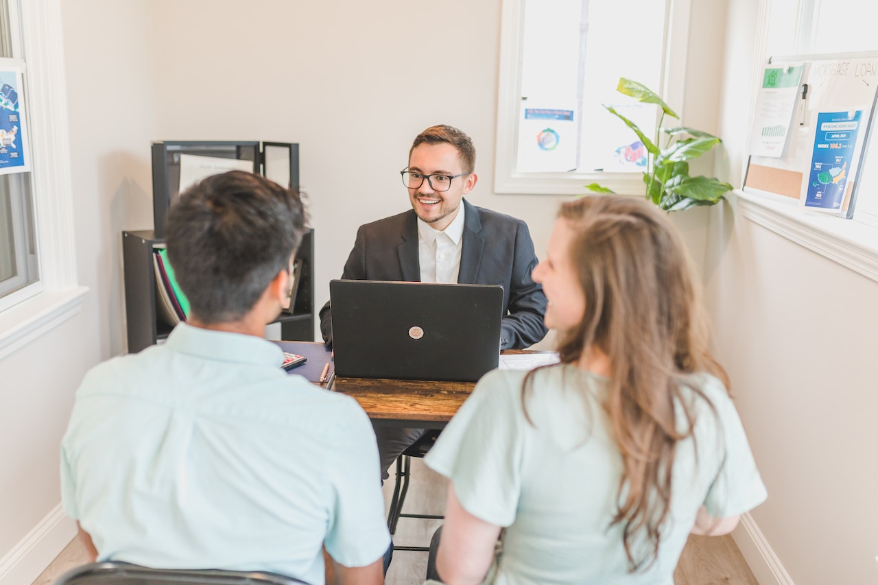 a couple and a realtor sitting at his office desk and talking