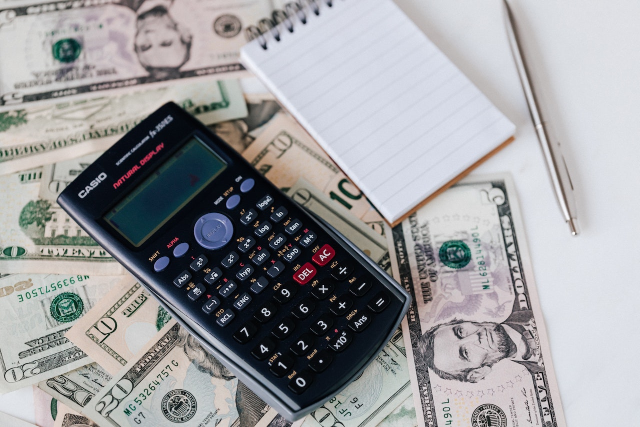 dollar bills, a calculator, a book note and a pen over a table