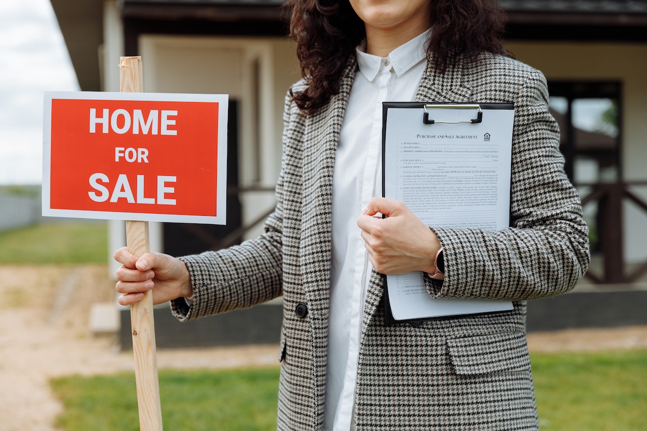 a realtor in front of a house holding a sign that says Home for Sale